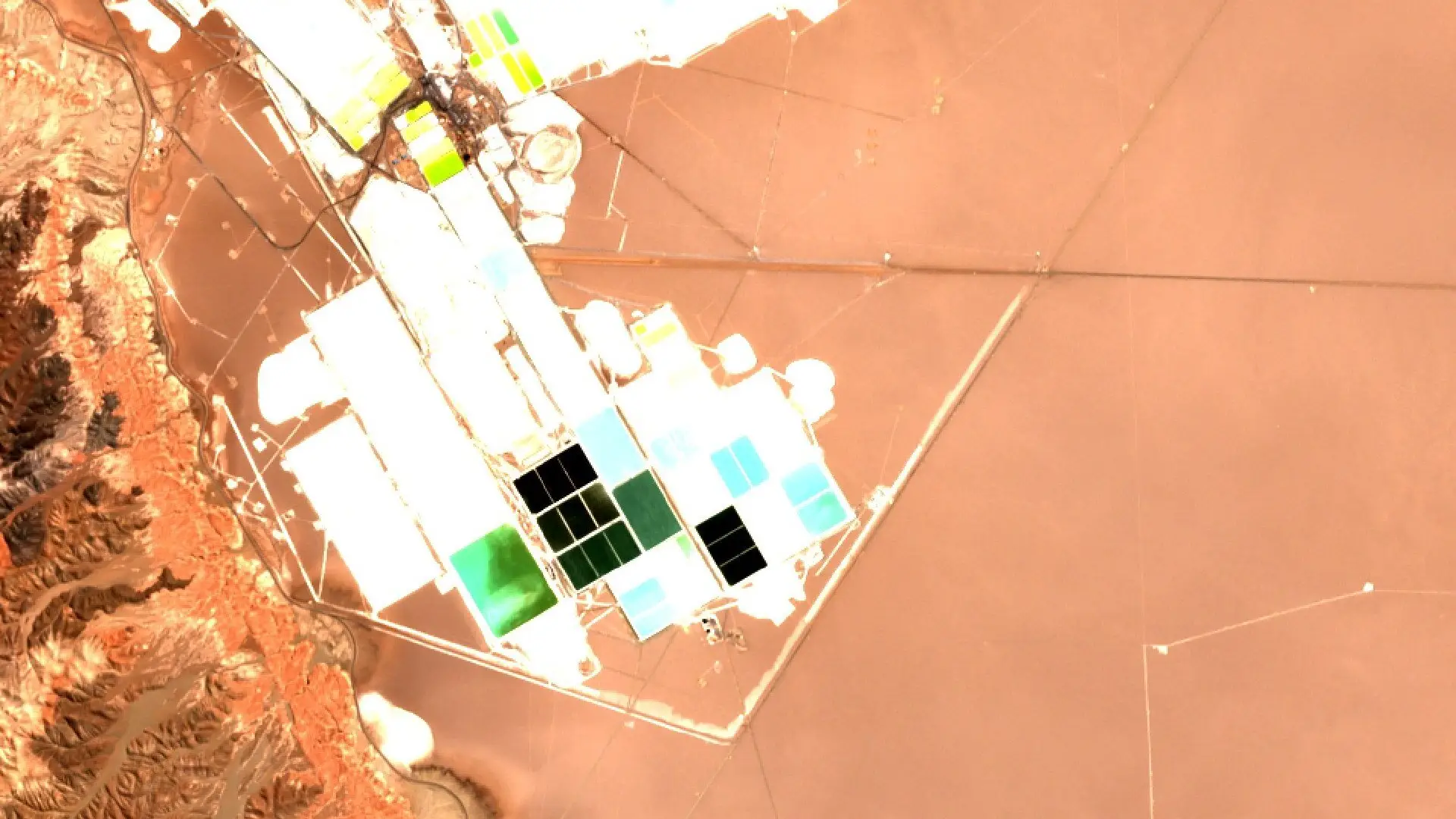 Sentinel-2 image of lithium and potash evaporation ponds at the edge of the Salar de Atacama, in white, pale blue, green and black rectangles beside a brown salt flat and eroded hills.