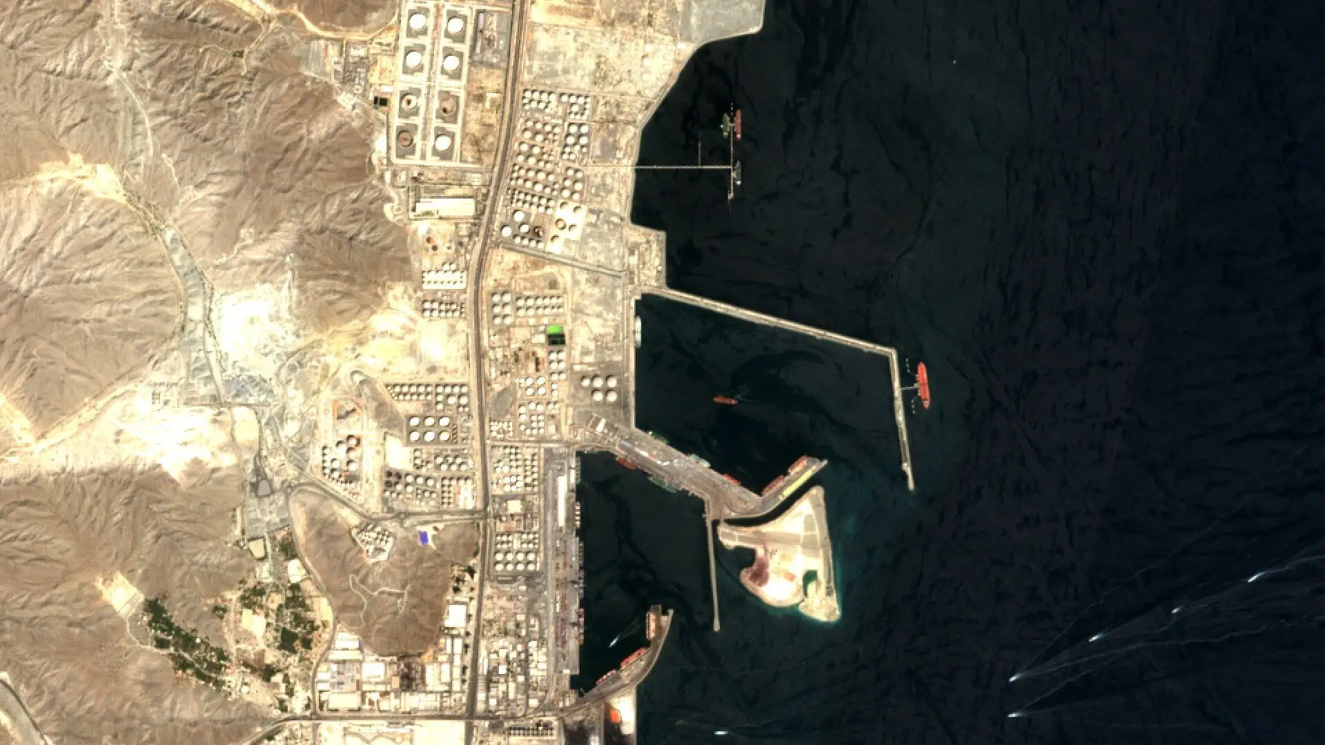 Sentinel-2 image of the Fujairah oil terminals, with rows of round storage tanks beside the coast road, a breakwater and tankers at berth beside the dark water of the Gulf of Oman.