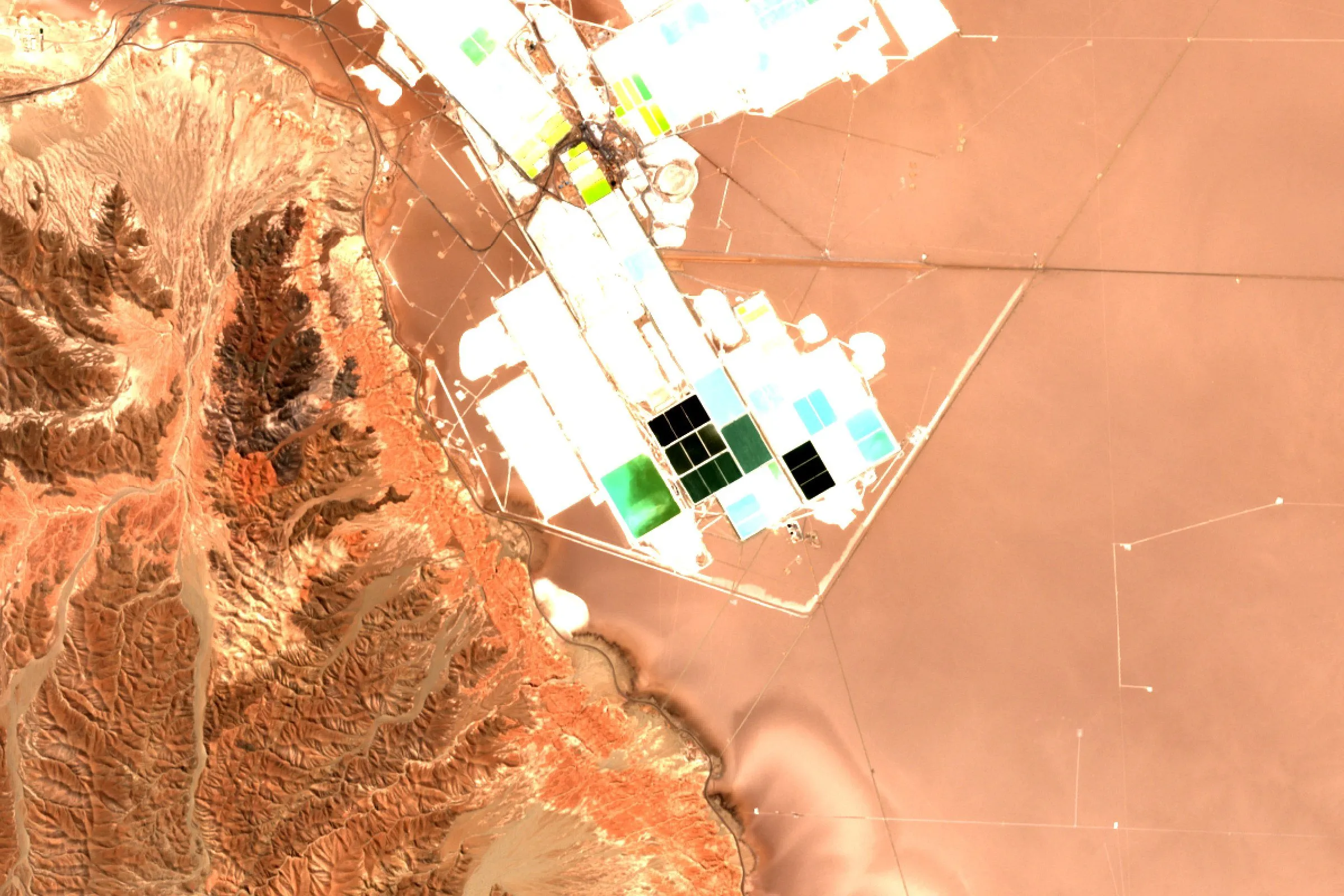 Satellite view of green, blue and white lithium evaporation ponds at the edge of a salt flat in the Atacama desert, Chile
