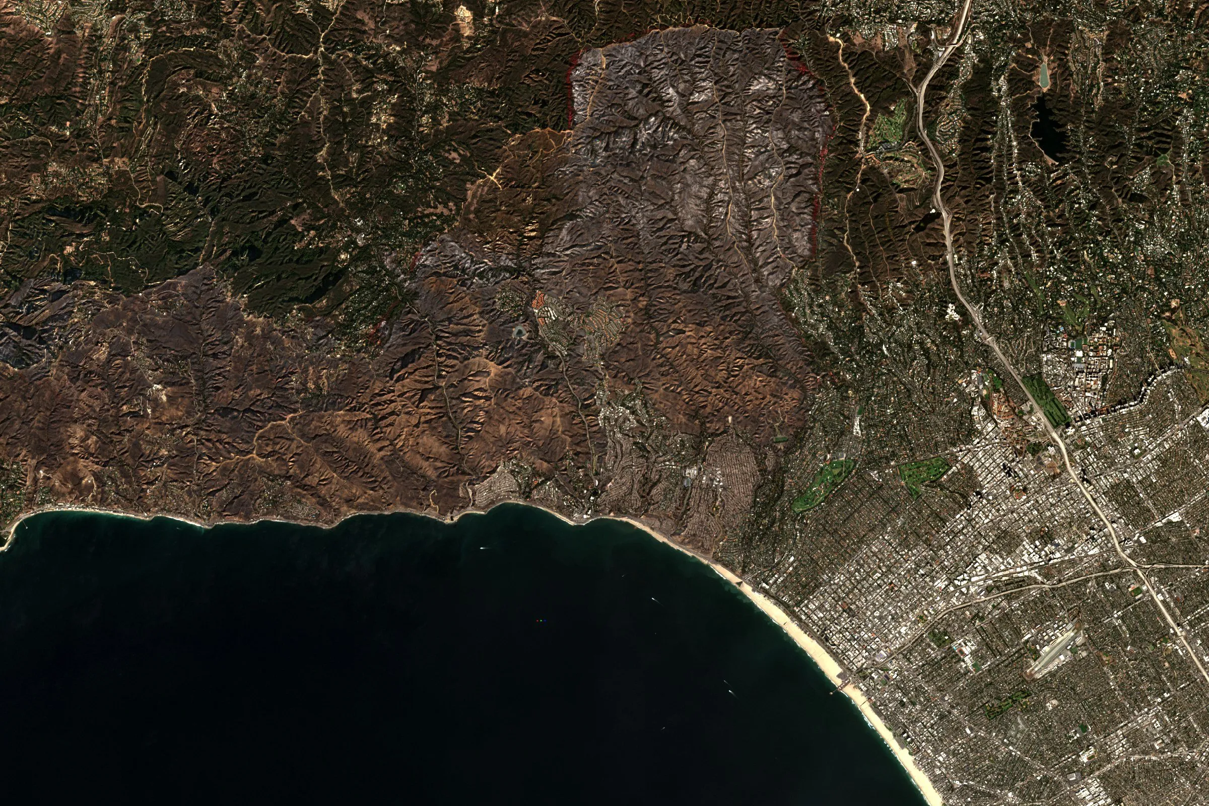 Satellite view of the Santa Monica Mountains above Los Angeles, with a dark wildfire burn scar behind the coast