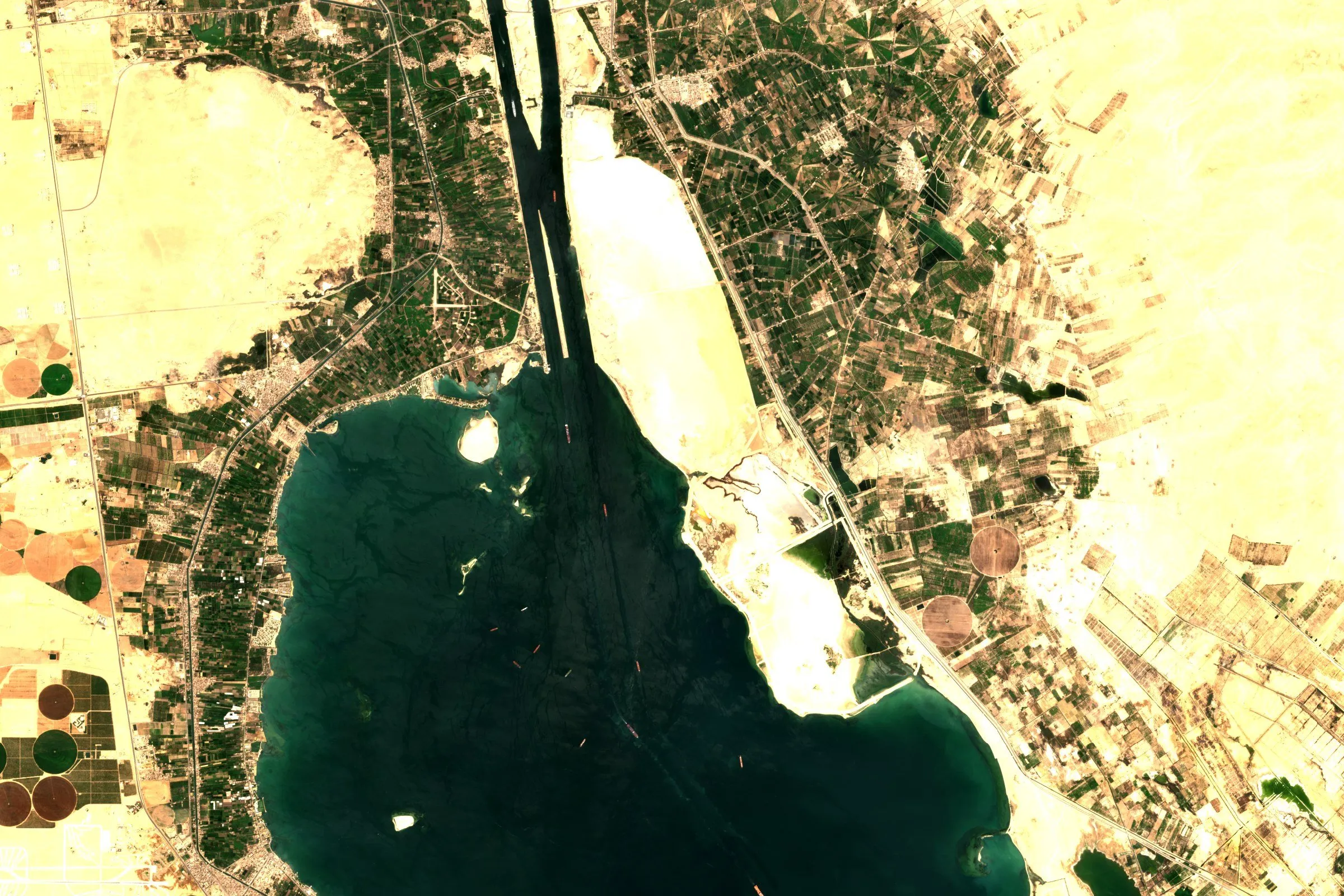 Satellite view of the Suez Canal and the Great Bitter Lake in Egypt, with ships in the channel and farmland on the banks